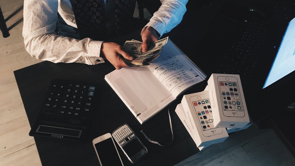 Persona haciendo cuentas con dinero y documentos financieros. ¿Por qué facturas tan pocas horas de todas las que realmente trabajas? — Compuasociados.