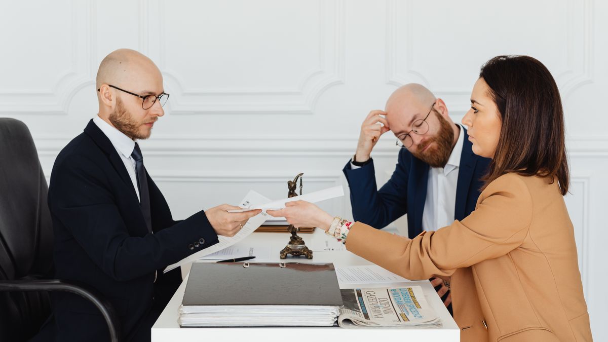 Abogado entregando un documento a sus clientes en una reunión. ¿Por qué tus clientes sienten que no les respondes aunque sí trabajes su caso? — Compuasociados.